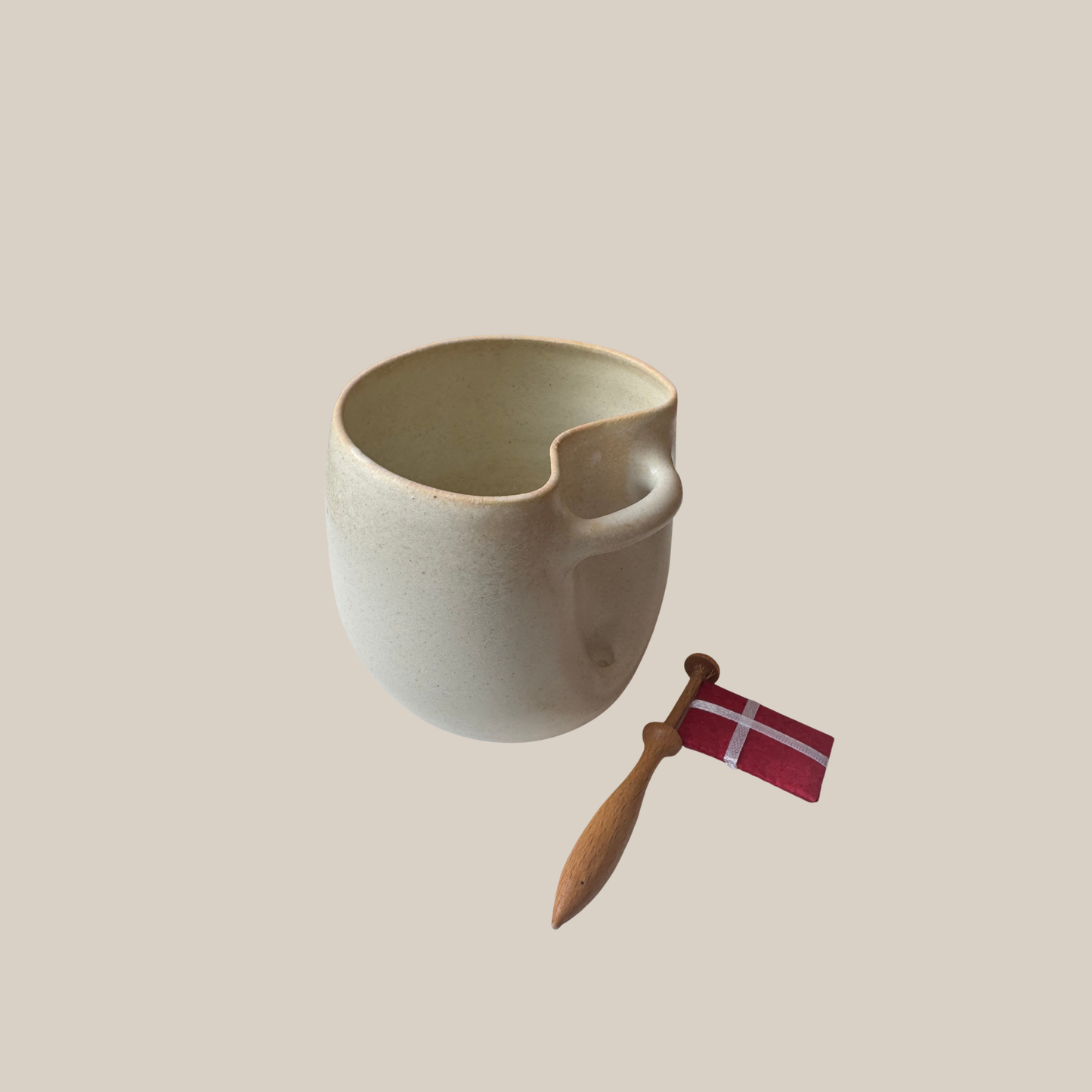Flødefarvet keramik kop med tilhørende flag.