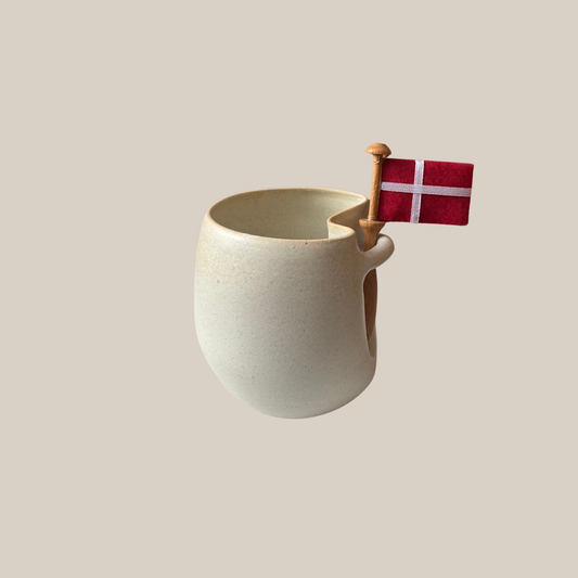 Flødefarvet keramik kop med tilhørende flag.